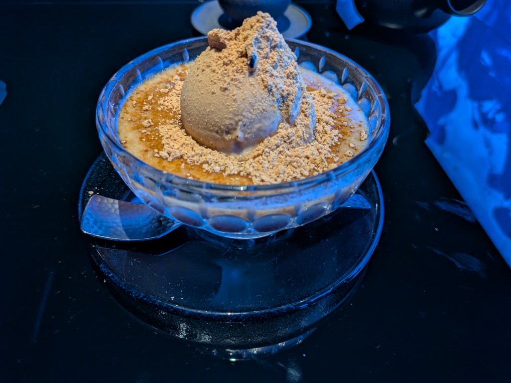 A bowl ot ice cream topped with a dusty beige powder, and sitting in a beige syrup