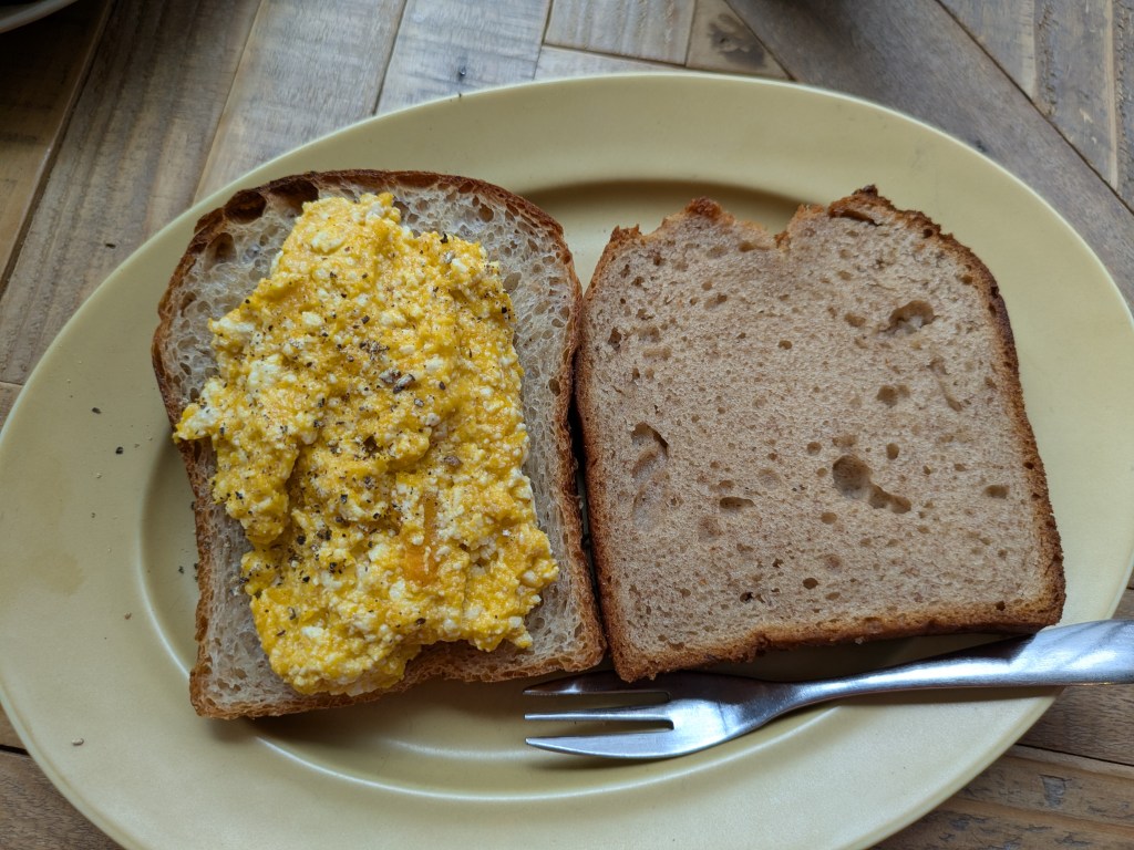 A slice of toast topped with scrambled tofu and a slice of banana bread