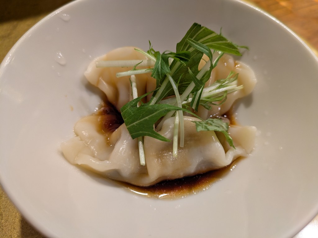 Two gyoza sitting in a little bit of dressing, topped with some greens