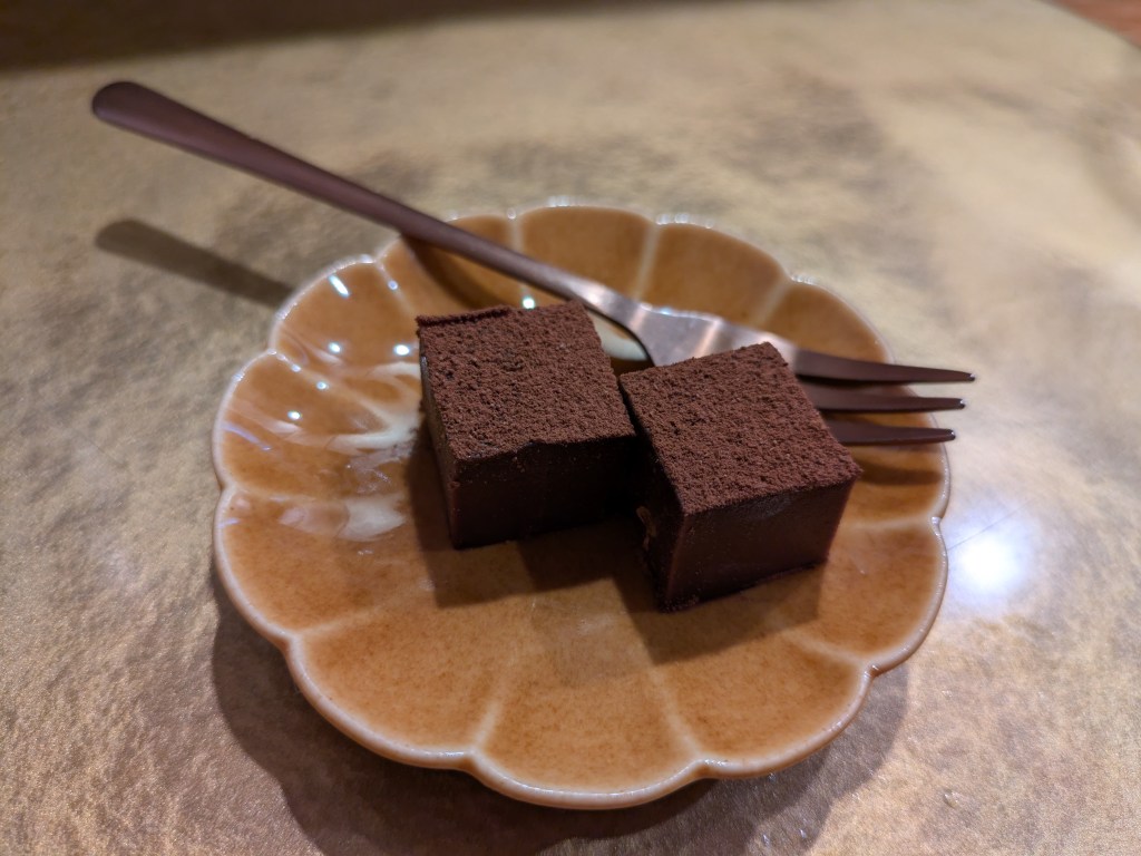Two small squares of chocolate truffle, topped with cocoa powder