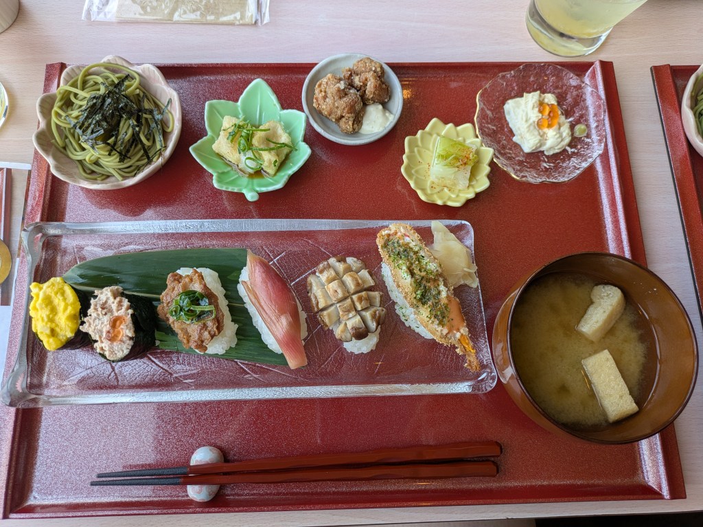 A tray with six pieces of sushi, five little side dishes, and a bowl of miso soup