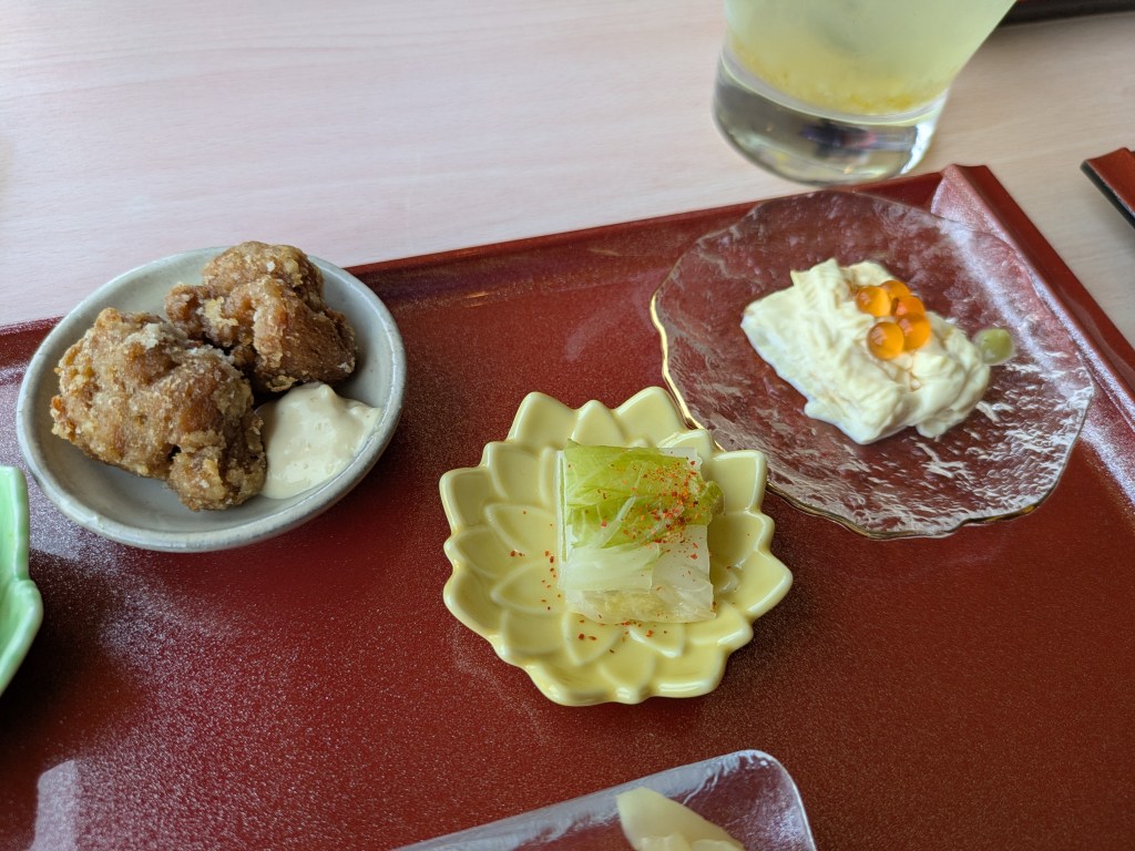 Three small dishes, one with fried vegan meat, one with pickled vegetables, and one with yuba 