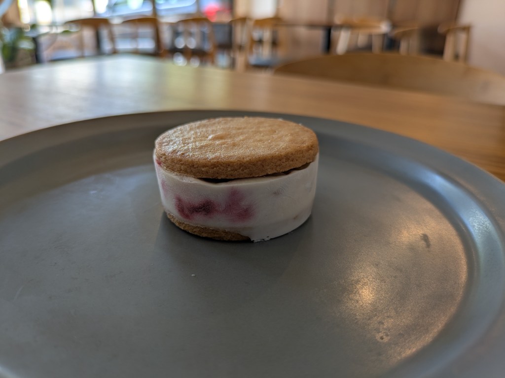 Two buttery biscuits with a pale ice cream sandwiched between them, with red berries visible in the ice cream