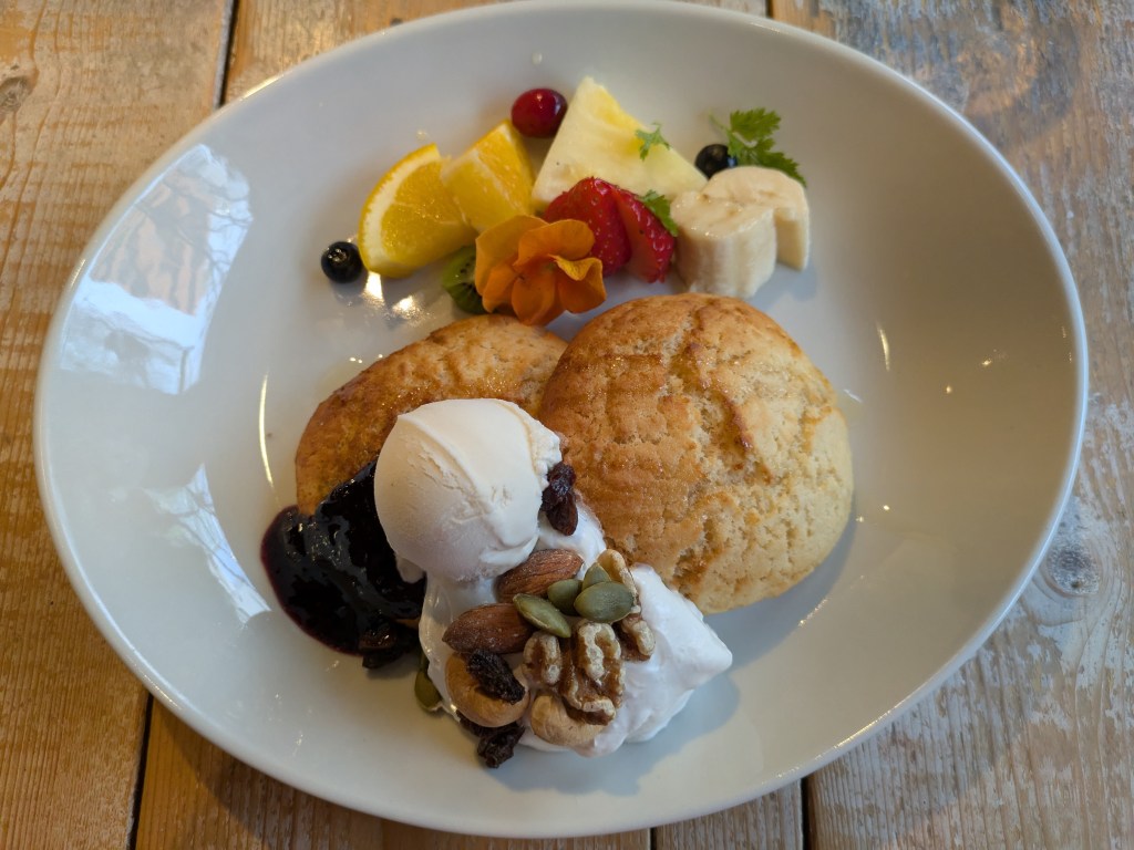 Two pillowy pancakes topped with ice cream  and cream and served with chopped fruit, compote, and nuts