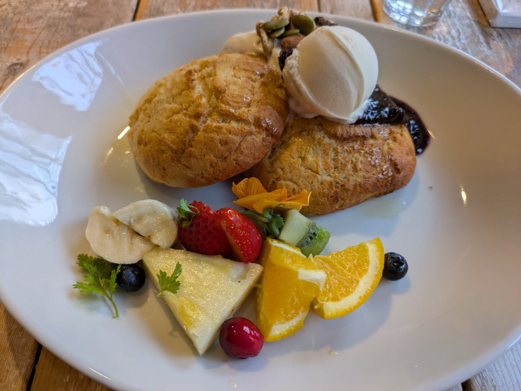 Two pillowy pancakes topped with ice cream  and cream and served with chopped fruit, compote, and nuts