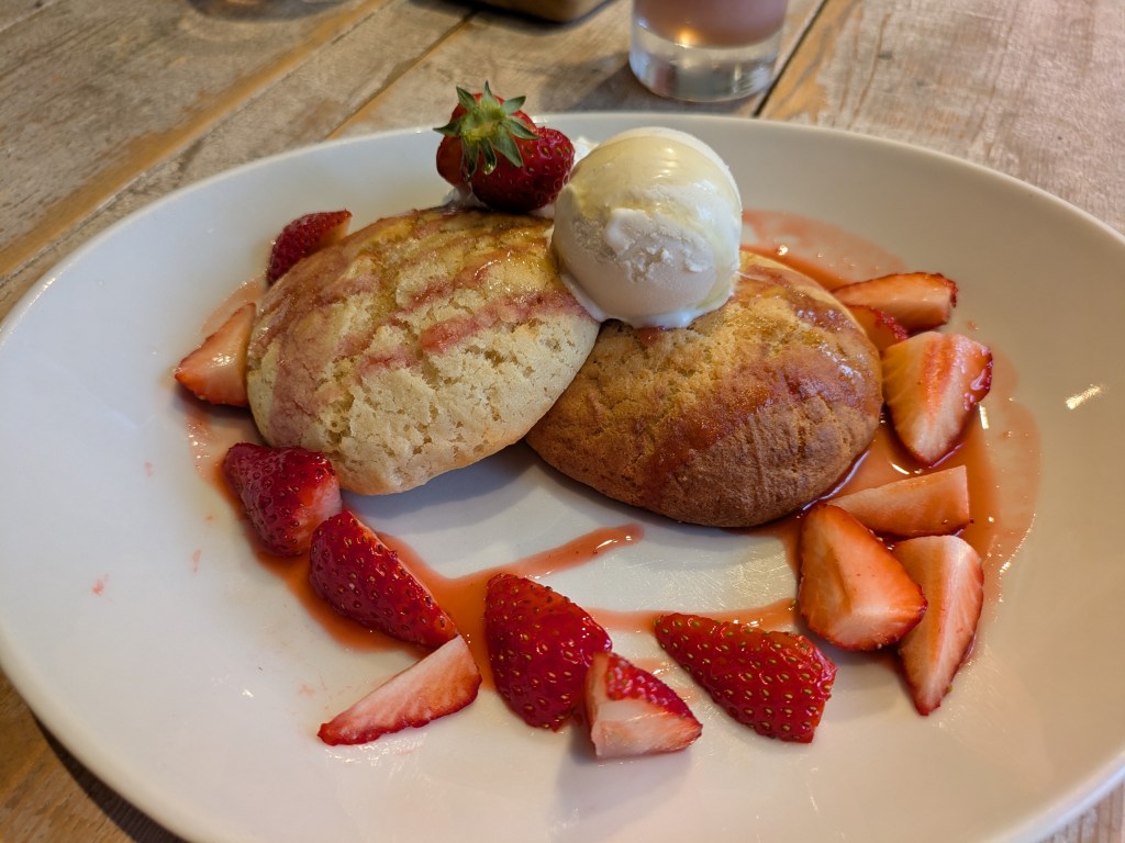 Two pillowy pancakes topped with ice cream and served with quartered strawberries and syrup