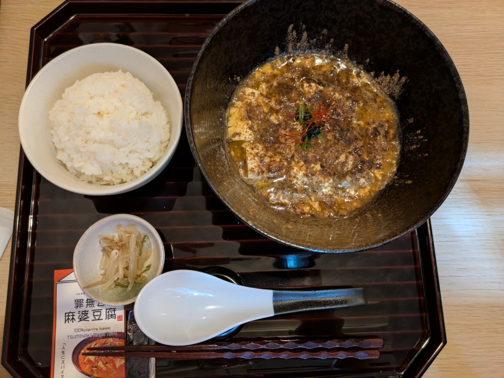 A tray with a bowl of rice, some pickled vegetables, and a large dish of mapo tofu