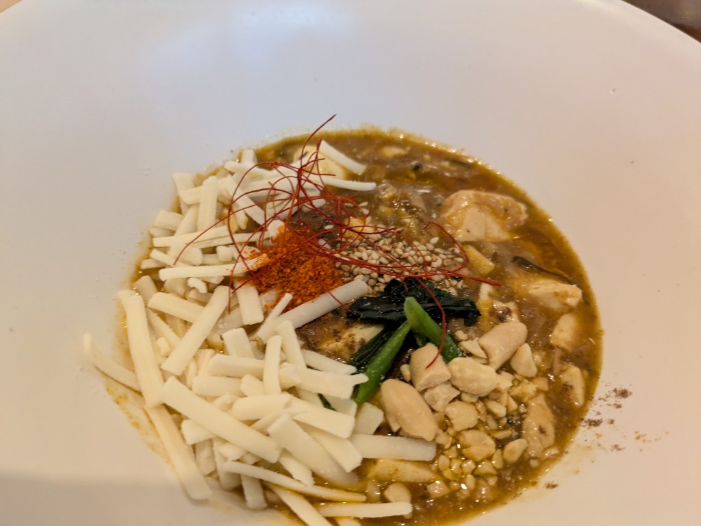 A curry sauce filled with tofu and vegetables, and topped with grated vegan cheese