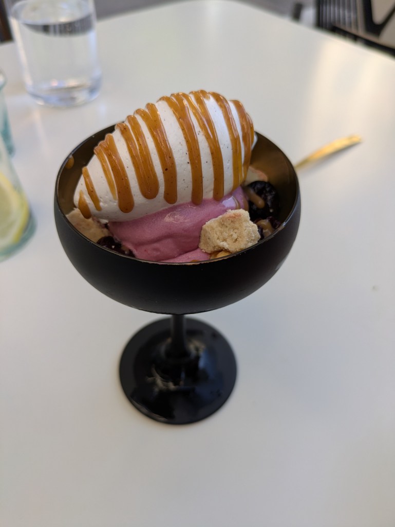 A bowl with pink ice cream, white ice cream drizzled with sauce, and bits of cookie and fruit