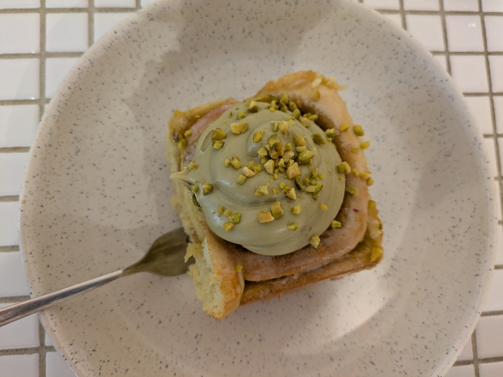 Cinnamon roll topped with a big dollop of pistachio cream and chopped pistachios