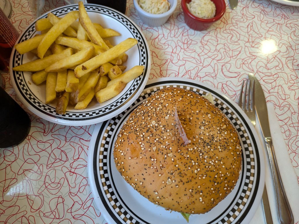 A bowl of chips and a big flat burger in a seeded bun