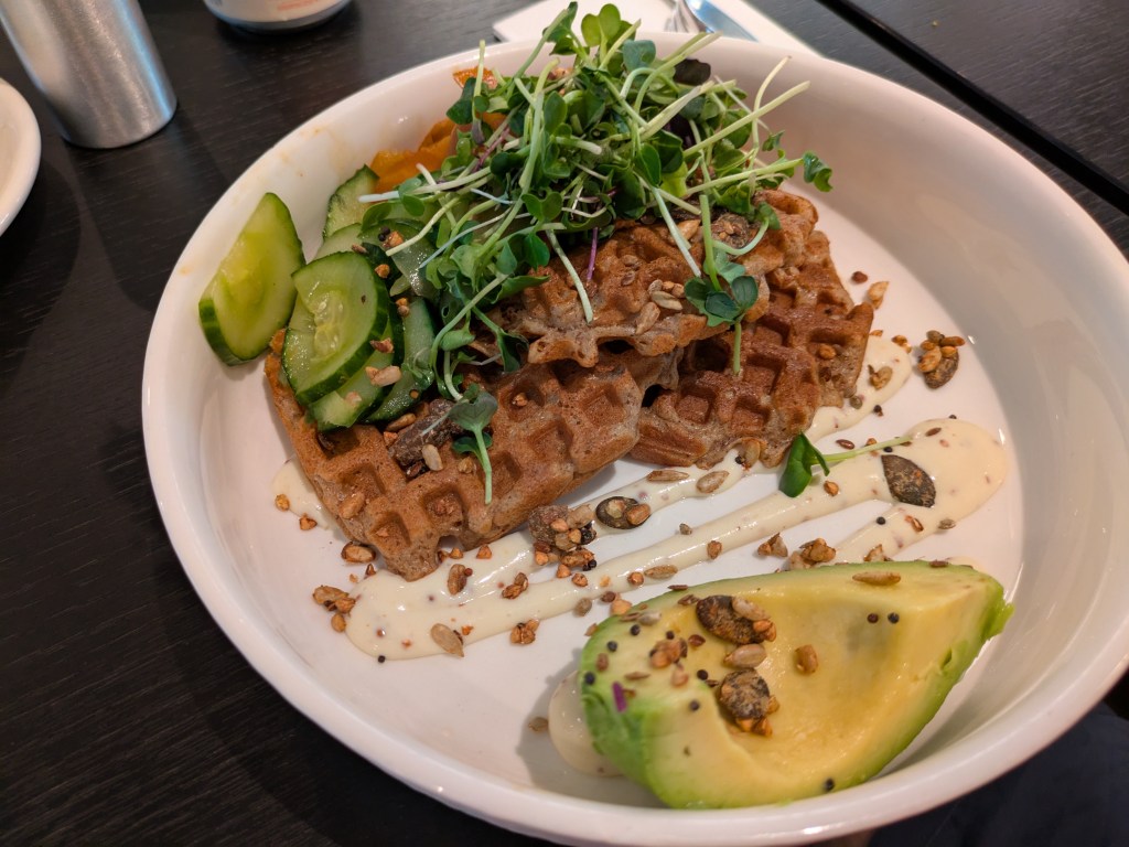 Three waffles topped with salad, served with cheesy dressing and avocado
