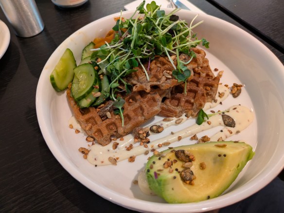 Three waffles topped with salad, served with cheesy dressing and avocado