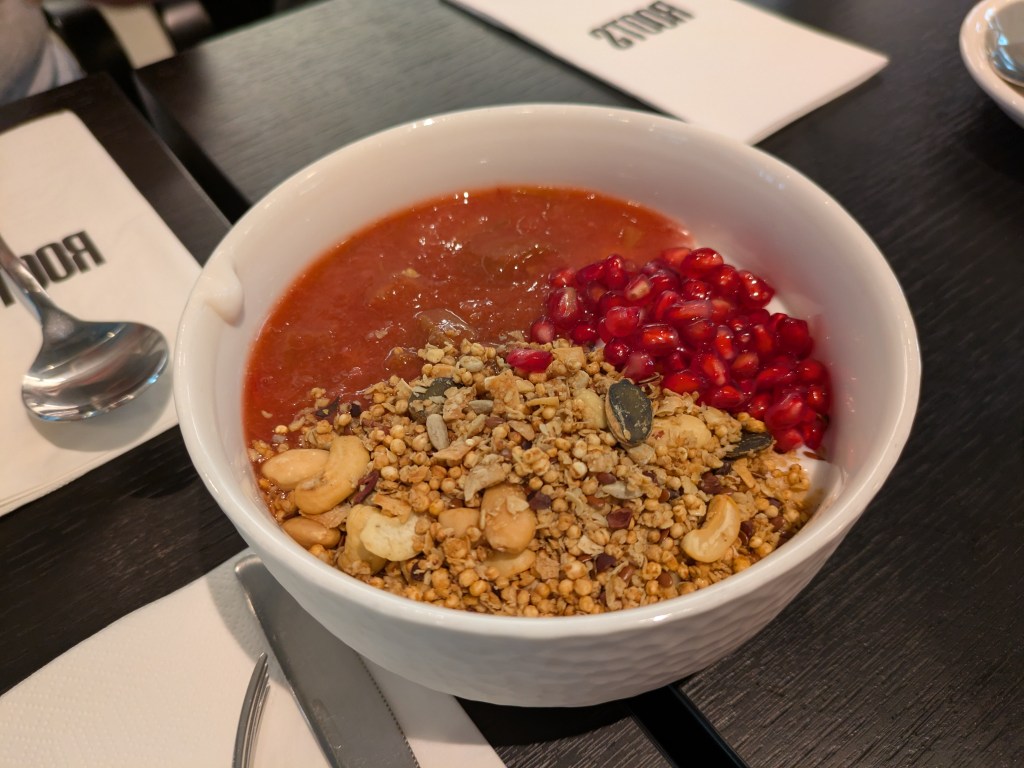 A large bowl of joghurt topped with granola, pomegranate seeds, and compote
