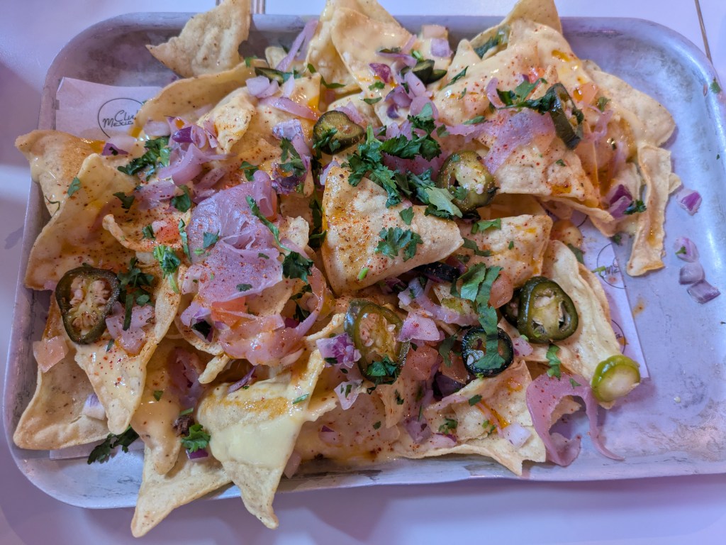 A tray of nachos with melted cheese and various seasonings
