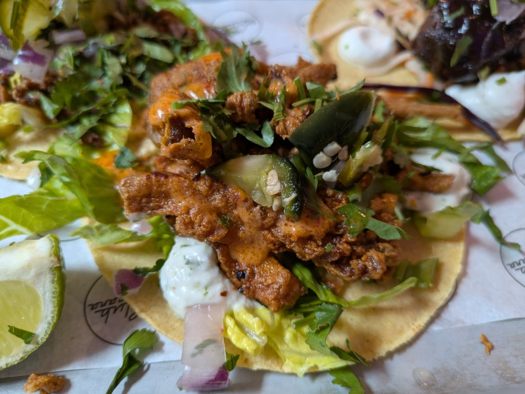 A taco with strips of battered mushrooms and various garnishes