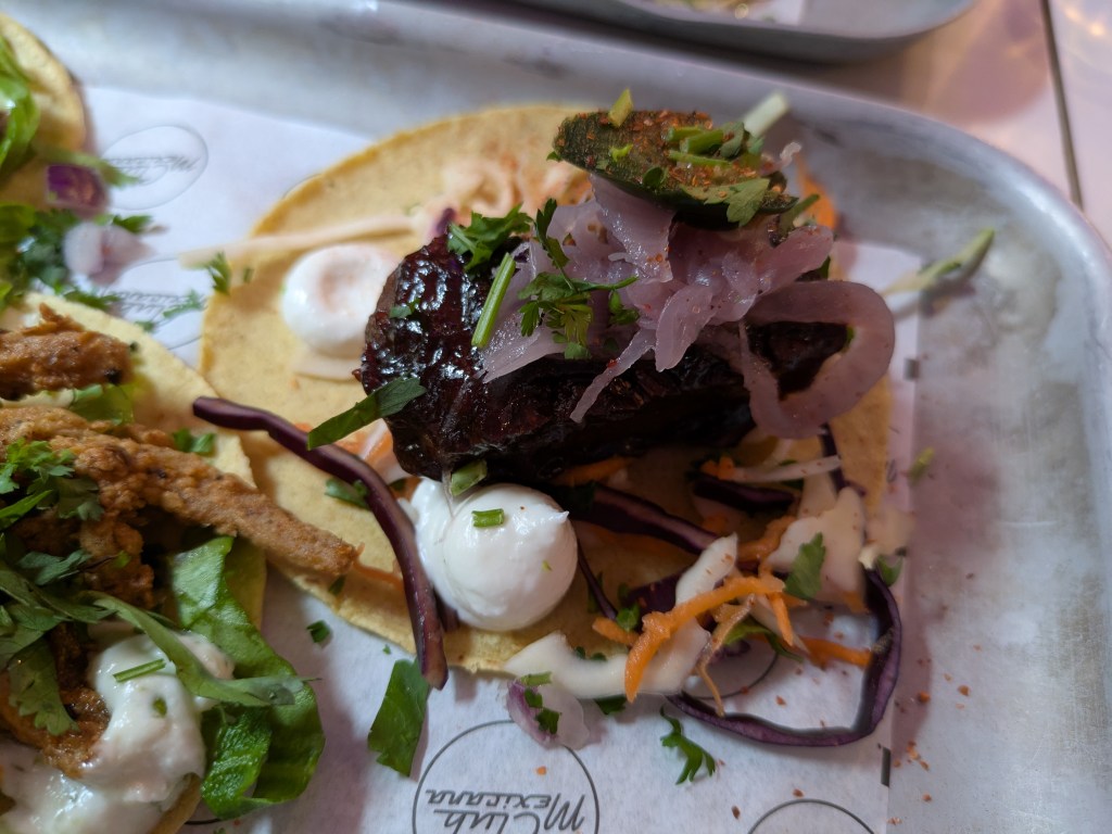 A taco with a large piece of mock meat, red onions, and other garnishes
