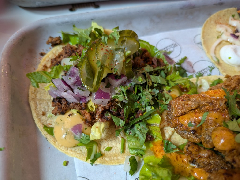A taco with mince, cheese sauce, red onion, pickles, and more garnishes