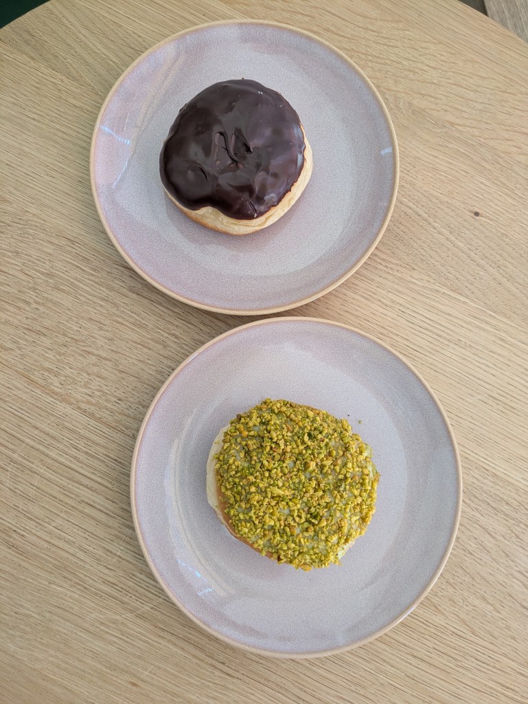 Two filled doughnuts, one covered in chocolate and the other with pistachios