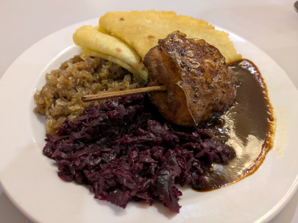 Two contrasting piles of cabbage, a big chunk of mock meat, some folded potato pancakes, and a rich gravy