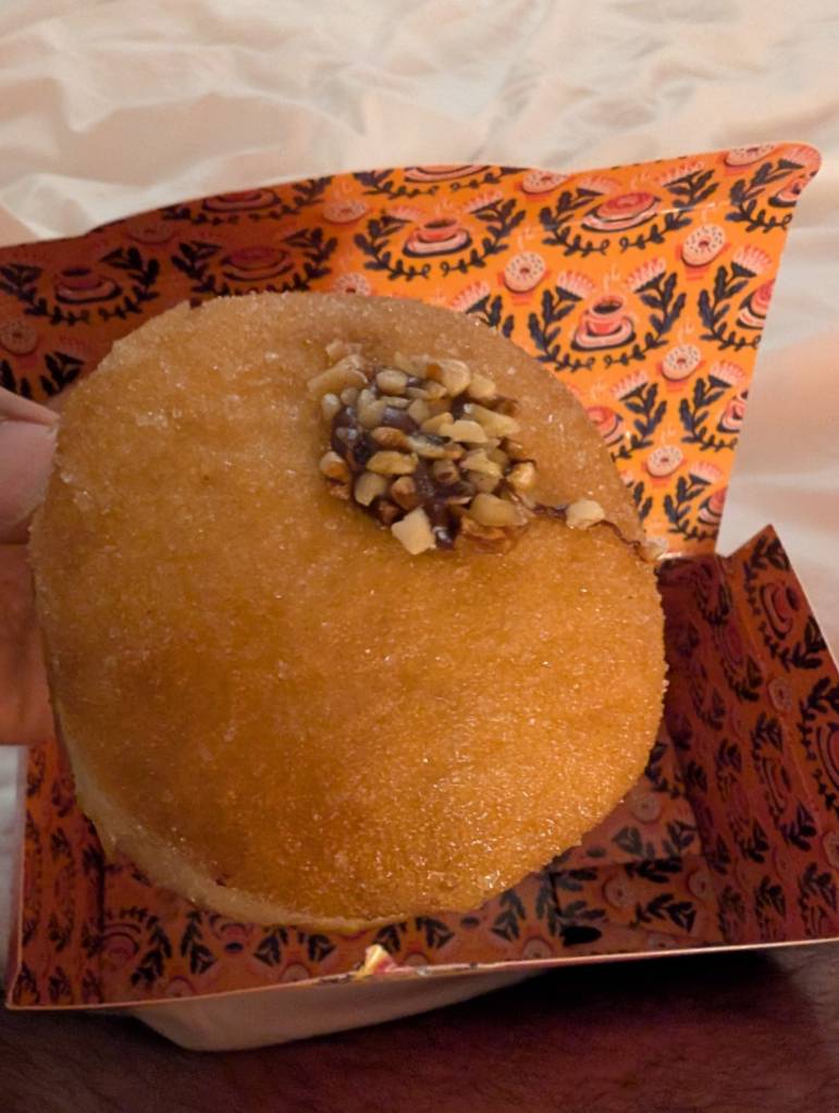 A plain looking filled doughnut with a small blob of chocolate and chopped hazelnuts on top