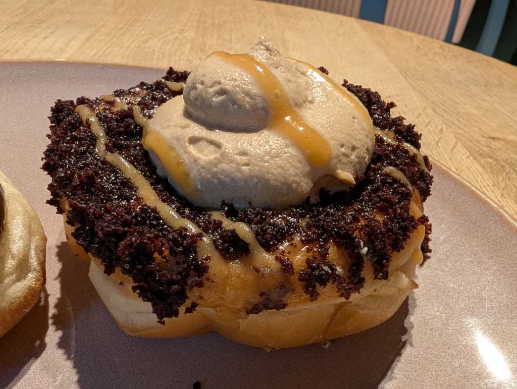 A doughnut topped with brownie crumbs, drizzled caramel, and a big scoop of cream