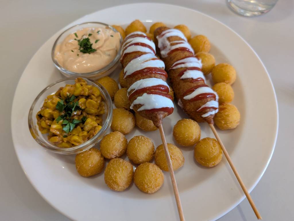 Two corn dogs with tater tots and accompaniments