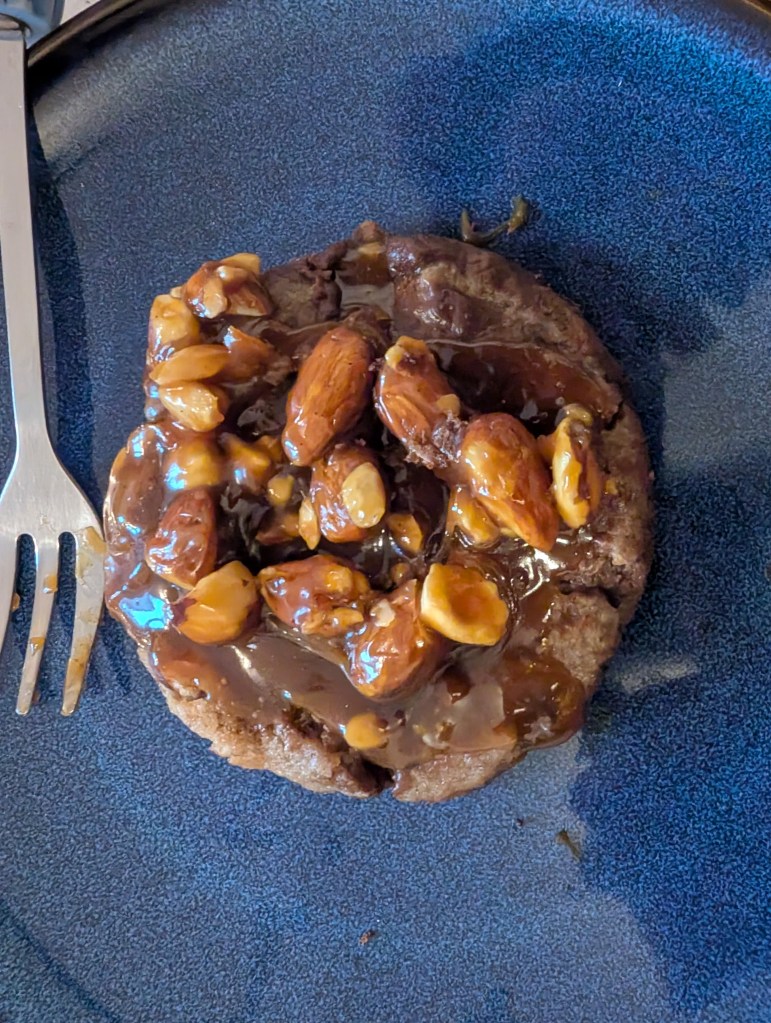 A chocolate cookie topped with sticky caramel and nuts