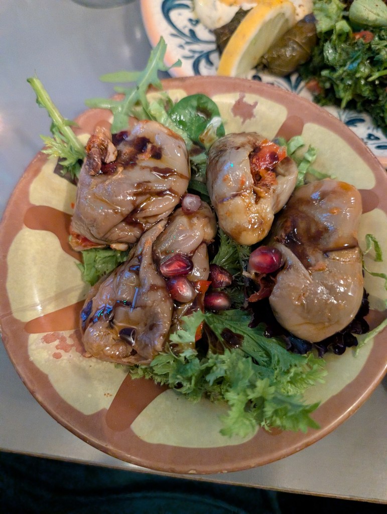 A plate of makdous, small pickled aubergine stuffed with walnuts. The dish is on a bed of salad and garnished with pomegranate seeds.