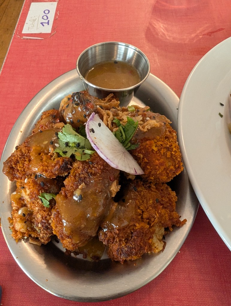 A plate of cauliflower wings with a crispy looking coating and a pot of sauce 