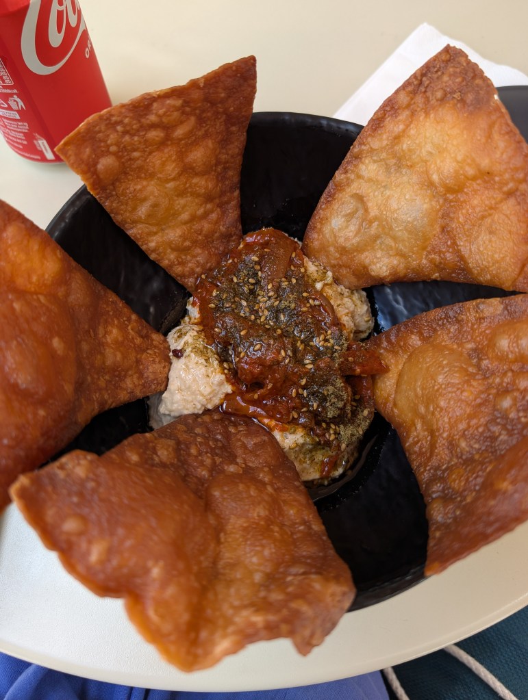 A bowl of kimchi hummus with some garnishes, and very well crisped tortilla chips