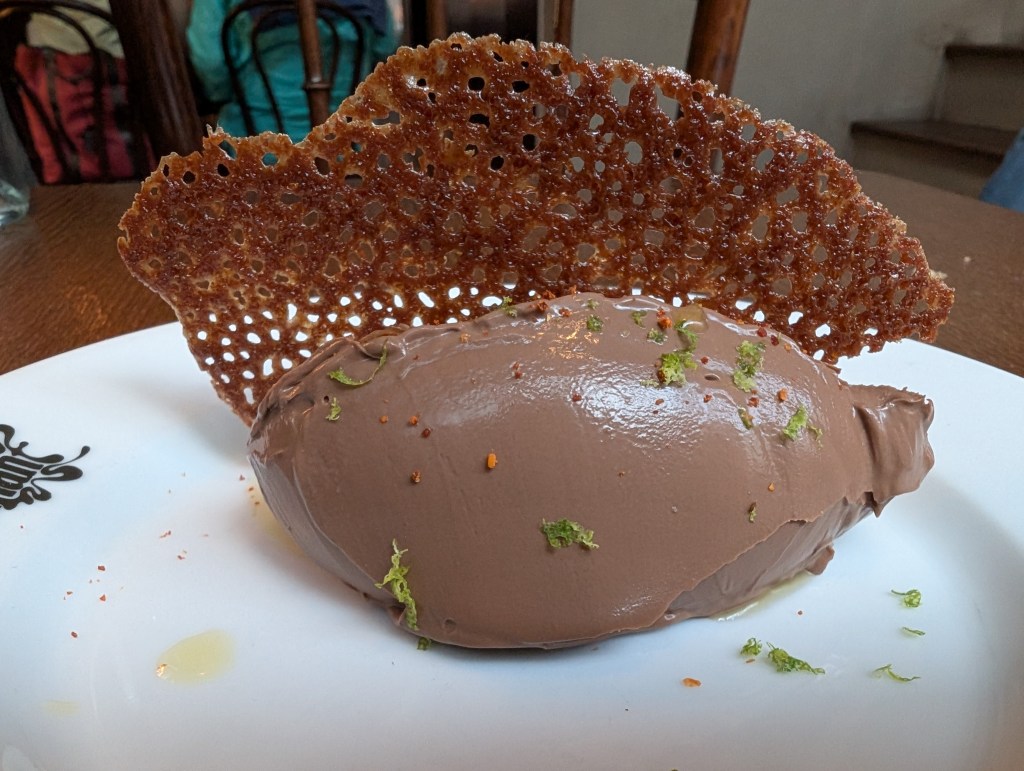 A quenelle of chocolate ganache garnished with lime zest and a tuile