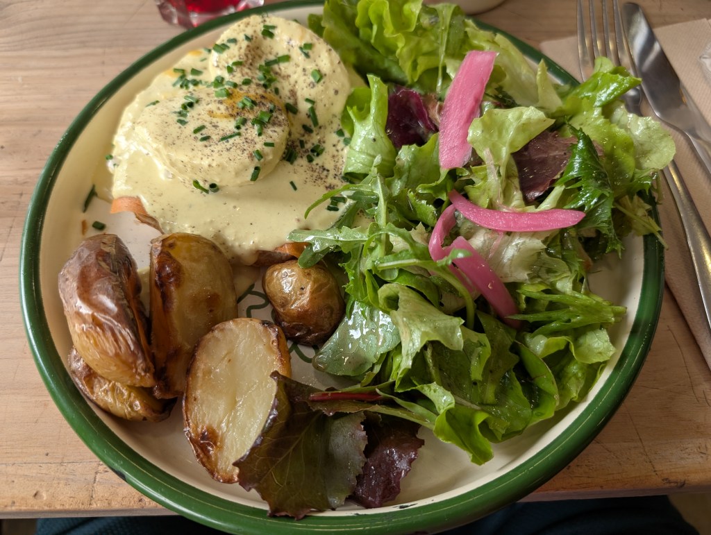 A plate with eggs Benedict, potatoes, and a lot of salad