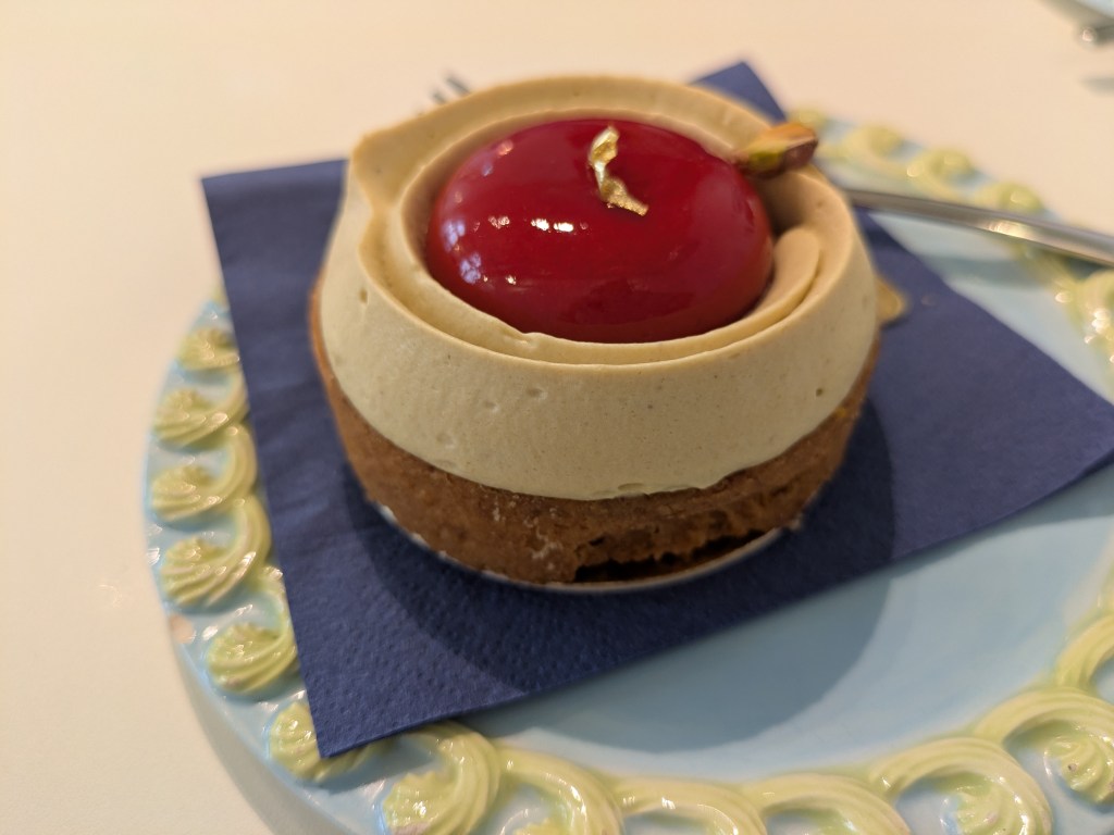 A pastry case topped with a glossy red dome encircled by a pale green pistachio cream