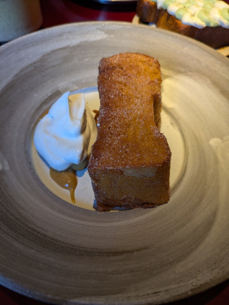 A long, thick slice of French toast alongside some fruit compote and a dollop of cream