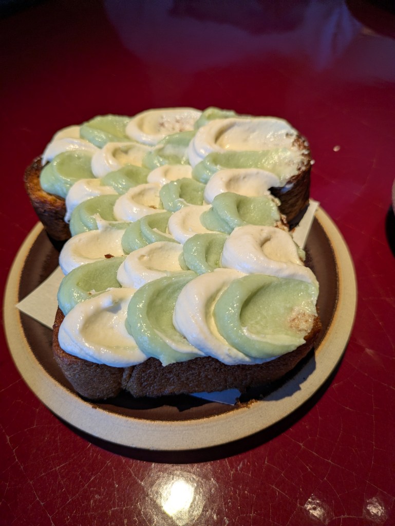 A large slice of brioche loaf topped with alternating artistic daubs of white coconut cream and green pandan cream