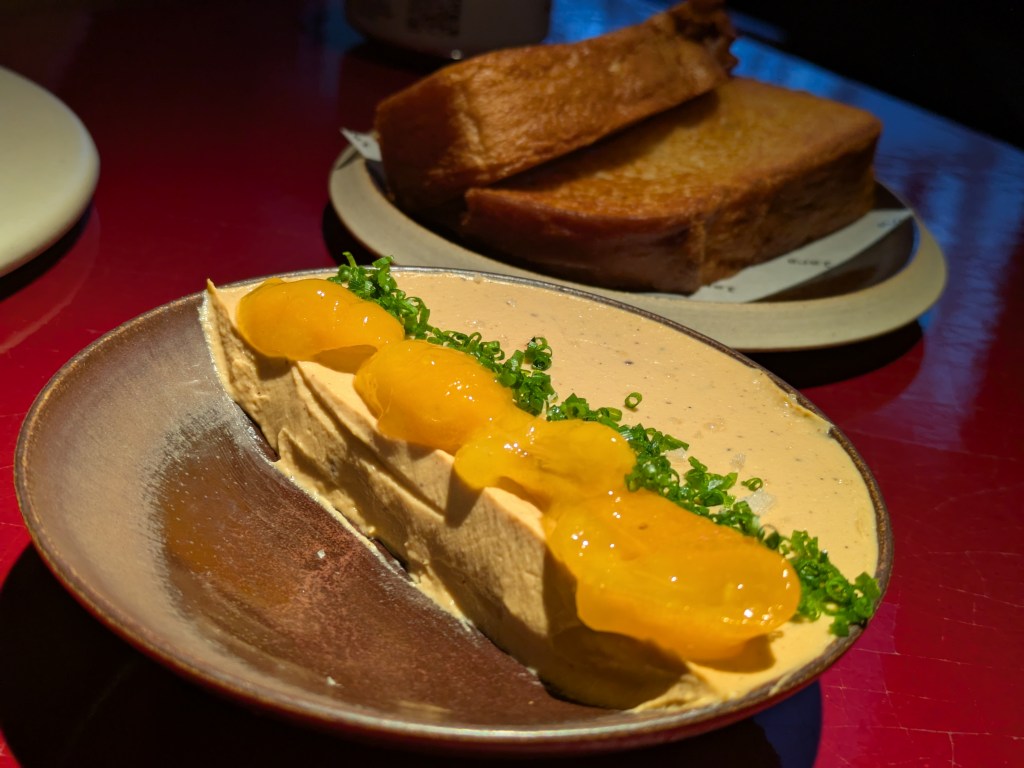 A dish of paté topped with kumquats and chives, with sliced brioche loaf in the background