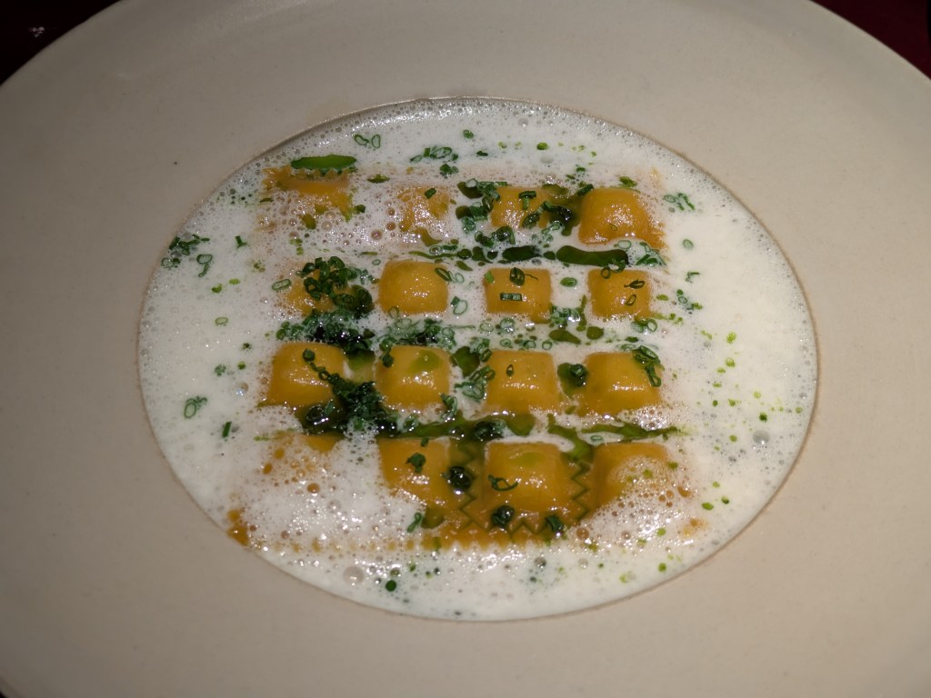A grid of small ravioli covered in white foam