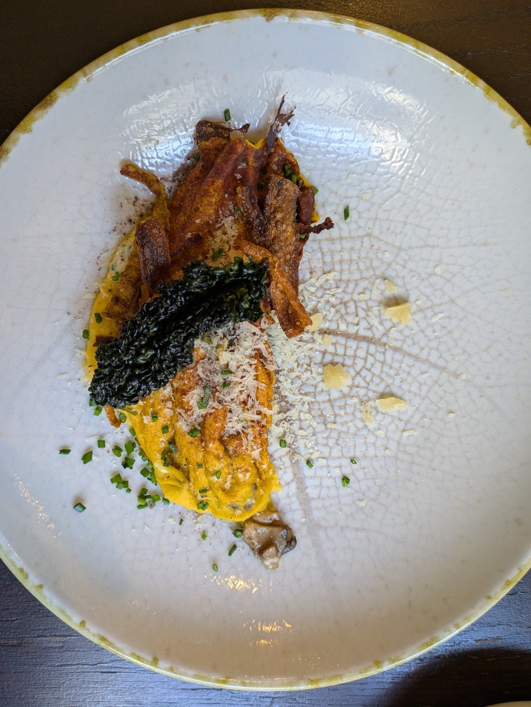 An omelette topped with cheese, herbs, and vegetable crisps