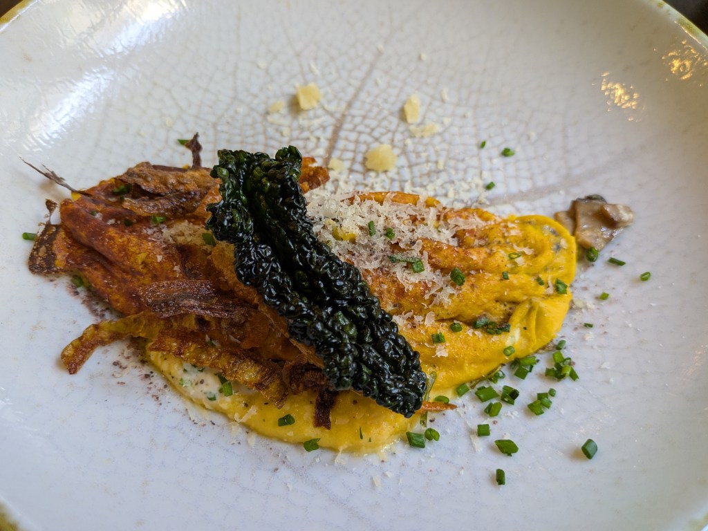 An omelette topped with cheese, herbs, and vegetable crisps