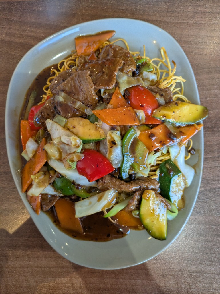 A big nest of crispy noodles topped with slivers of mock beef, big pieces of veg, and sauce