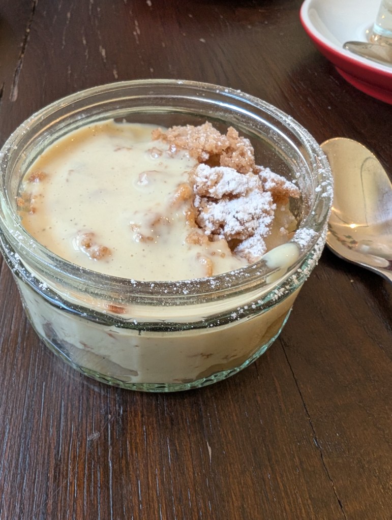 A pot of apple crumble with some custard poured in 
