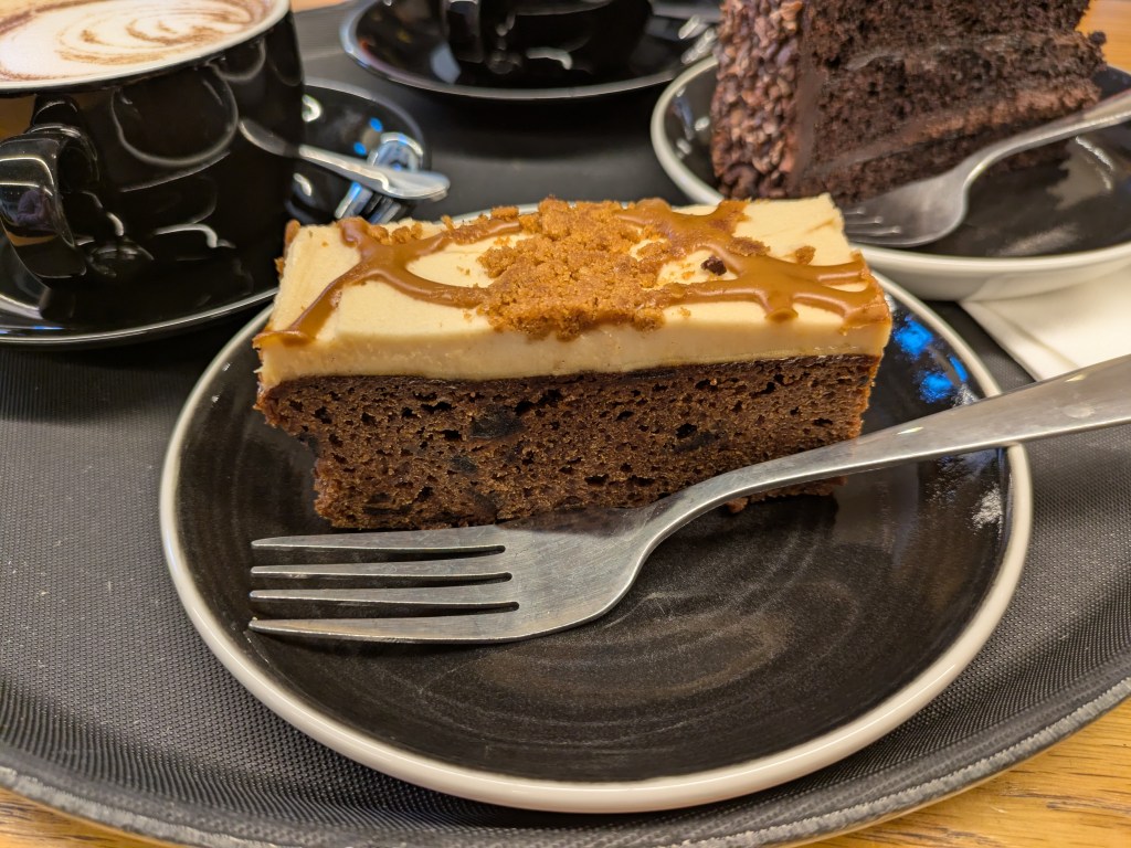 A thick rectangular slice of cake with a creamy icing drizzled with toffee sauce 