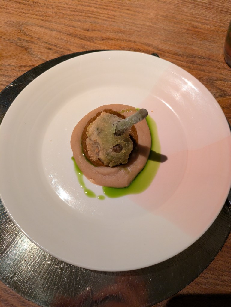 A crispy fried artichoke on top of a tomato puree, white bean purée, and vivid green oil