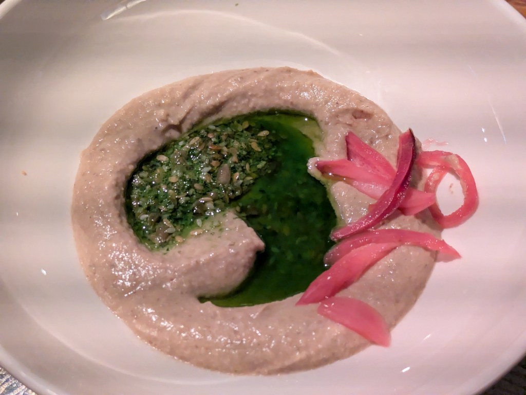 A smooth white puree topped with green pesto and oil and bright pink pickled onions