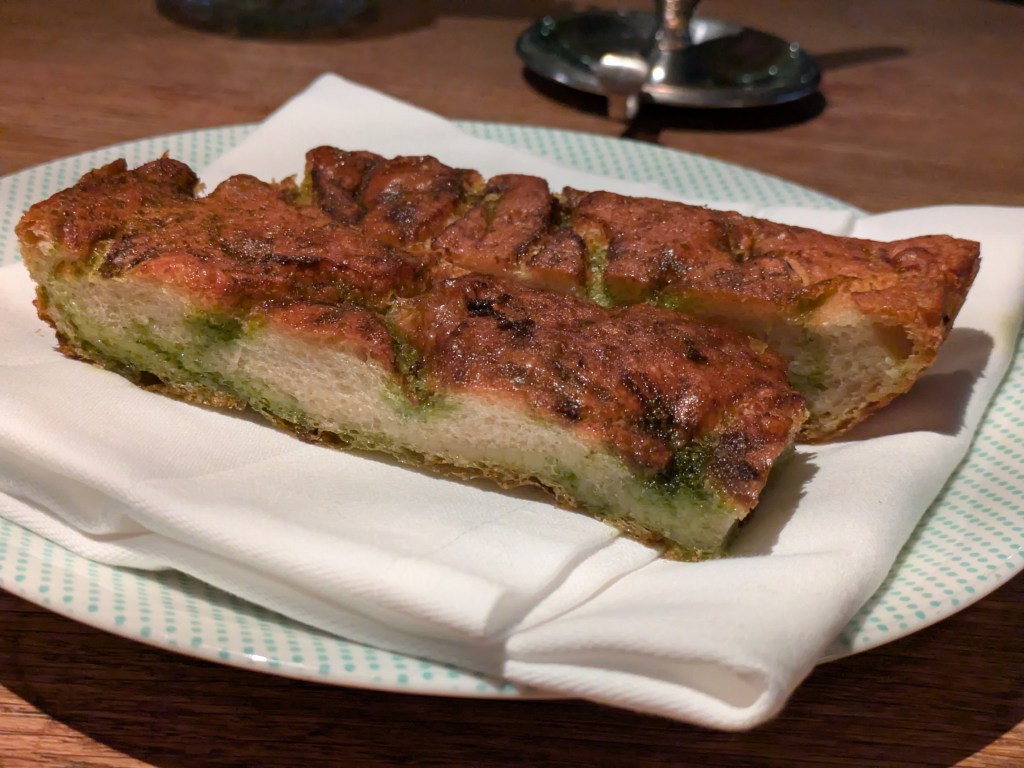 Two slices of focaccia with a crispy top and herby green oil running through it