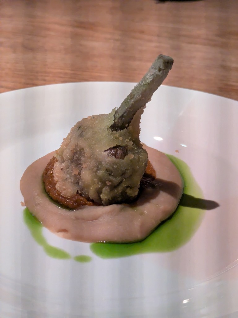 A crispy fried artichoke on top of a tomato puree, white bean purée, and vivid green oil