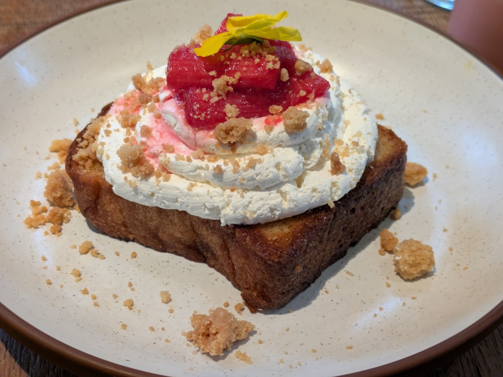 A thick slice of French toast topped with a generous spiral of cream and some pink rhubarb
