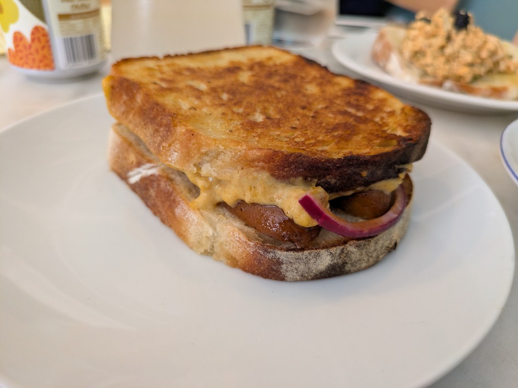 A toasted sandwich filled with sausage, cheese sauce, and red onion