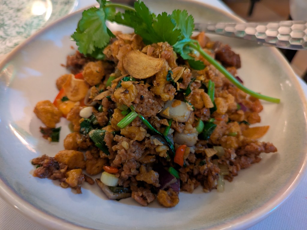 A dish with several different types of vegan pork, in mince form and small chunks, with chillies, vegetables and herbs